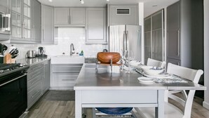 A modern kitchen with grey cabinets, stainless steel appliances, and a central island with a wooden bowl. - Villa Nautilus, Nautilus on Sapphire Beach (Charlotte Amalie)