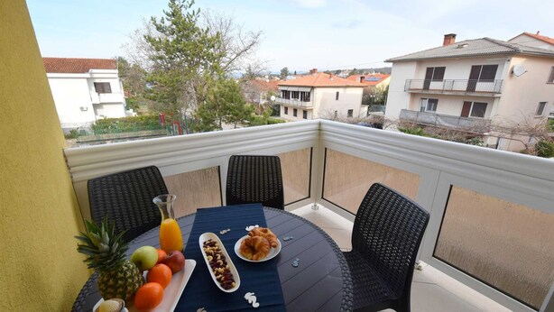 Un balcón con una mesa redonda dispuesta para el desayuno, con frutas, frutos secos y croissants.