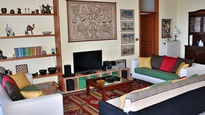 Ein Wohnzimmer mit Fernseher, zwei Sofas, einem Couchtisch und einem Bücherregal mit diversen Gegenständen.