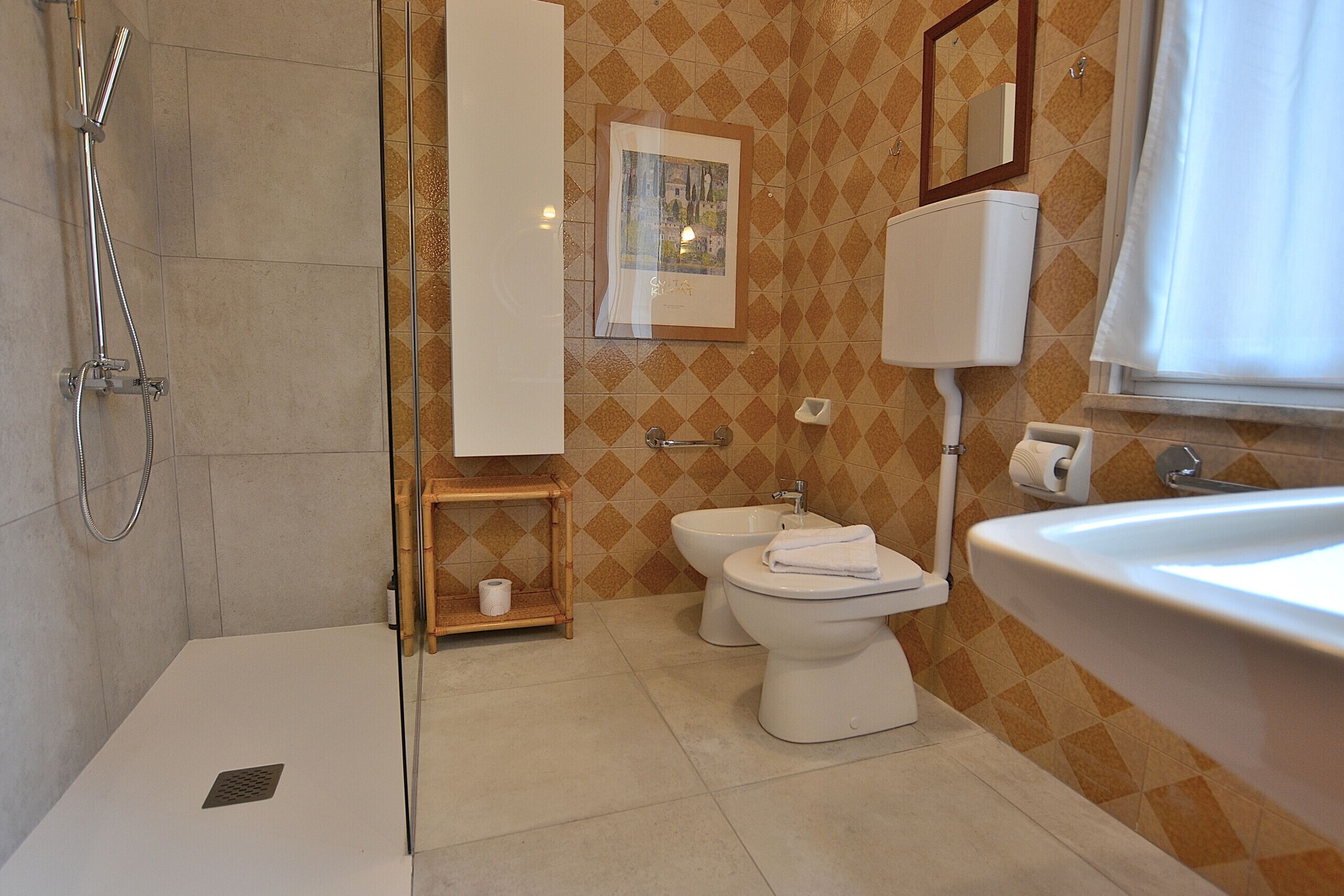 A bathroom with a shower, two toilets, a sink, and a framed picture on the wall.