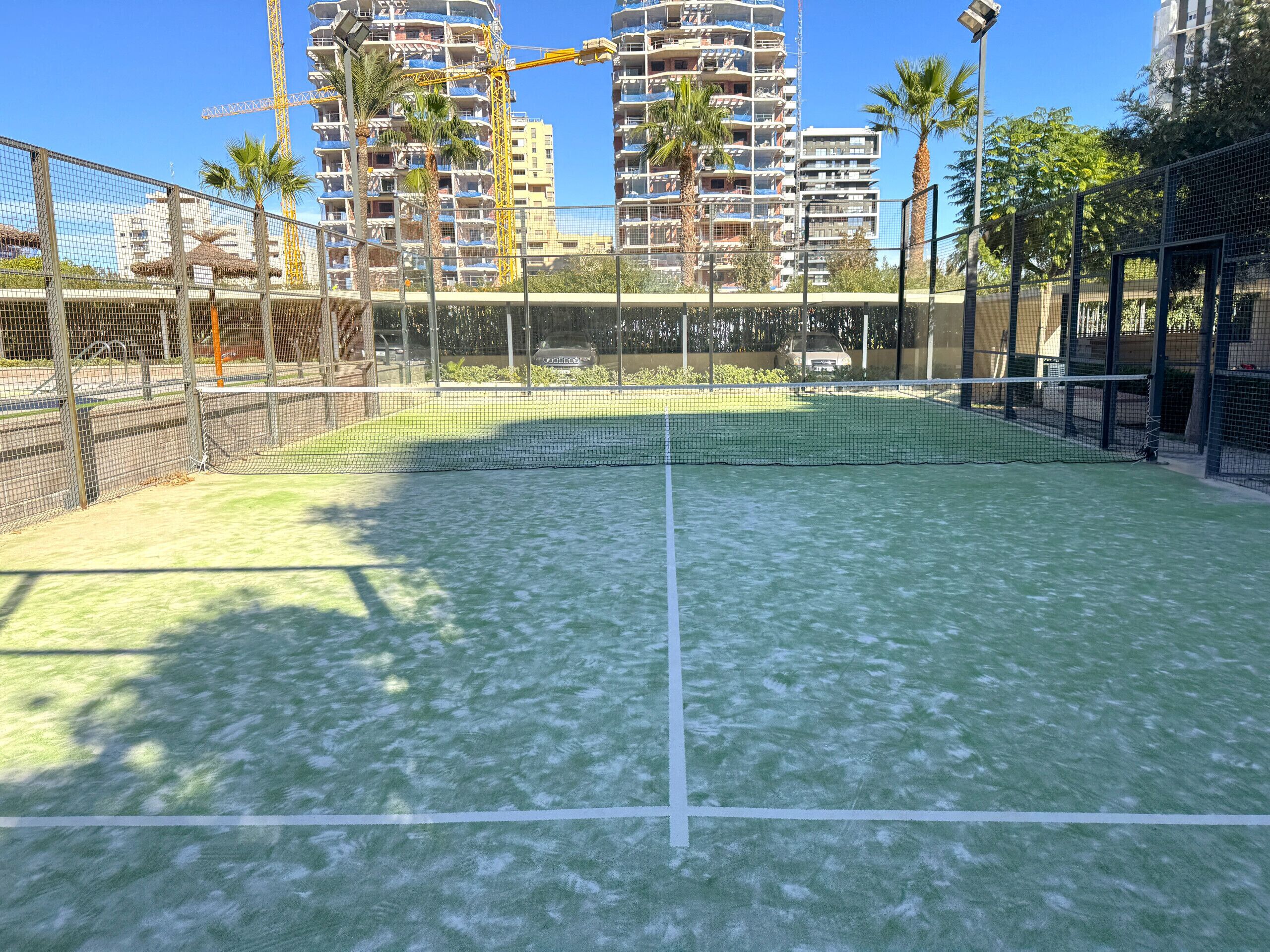 Un campo da tennis con rete, circondato da una recinzione e palme.