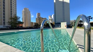 A swimming pool with clear water and metal pool ladders, surrounded by tall buildings and a clear sky. - MIRADORBEACH-1ºlínea Playa-Wifi y Garaje Gratis. (Calpe / Calp)