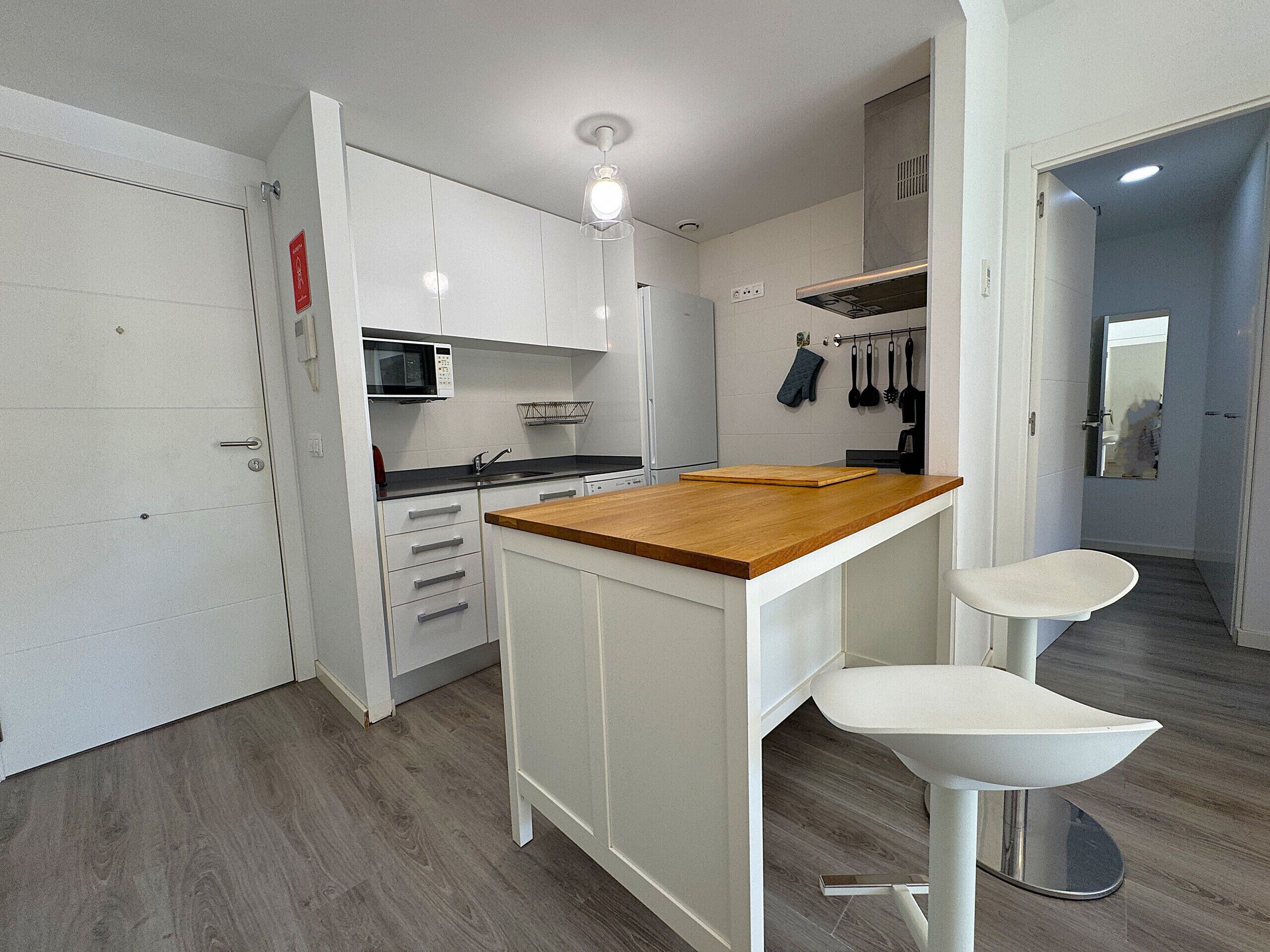 Une cuisine de taille réduite avec des meubles blancs, un plan de travail en bois et un évier.