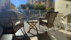A balcony with wicker chairs and a small table, overlooking a cityscape with tall buildings and palm trees. - MIRADORBEACH-1ºlínea Playa-Wifi y Garaje Gratis. (Calpe / Calp)