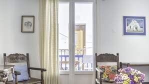 Een kamer met twee houten stoelen, een tafel, een vaas met bloemen en twee foto's in lijsten aan de muren.