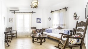 Een woonkamer met een houten vloer, een bank, een schommelstoel, een salontafel met bloemen en een eettafel met stoelen.
