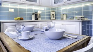 Een keuken met witte kastjes, blauwe tegels en een houten tafel met witte kommen en kopjes.