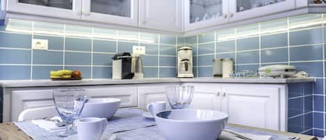 A kitchen with white cabinets, blue tiles, and a wooden table with white bowls and cups.