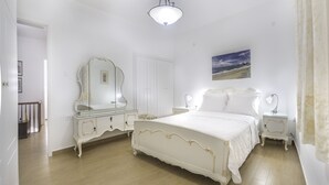 Een slaapkamer in witte tinten, met een groot bed, een kaptafel en een spiegel.