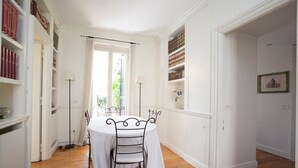 Uma área de refeições com uma mesa redonda e cadeiras, cercada por paredes brancas e piso de madeira.