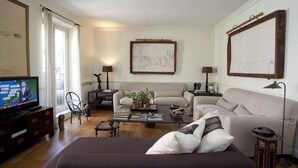 Uma sala de estar com televisão, sofás, mesa de centro e obras de arte nas paredes.