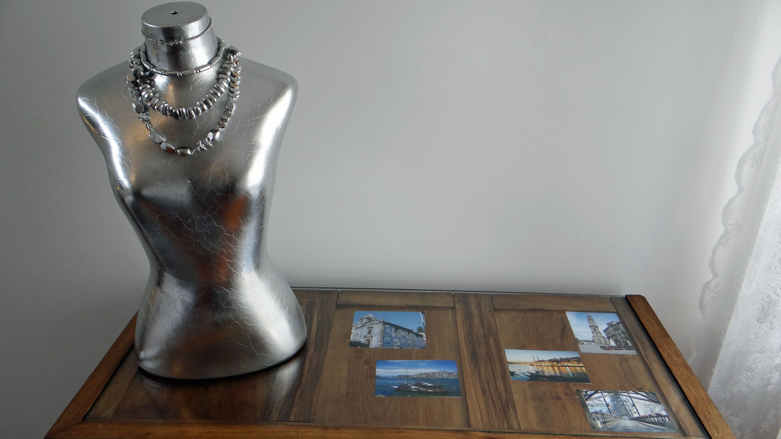 A mannequin with a silver dress and a necklace on a wooden table with framed pictures.