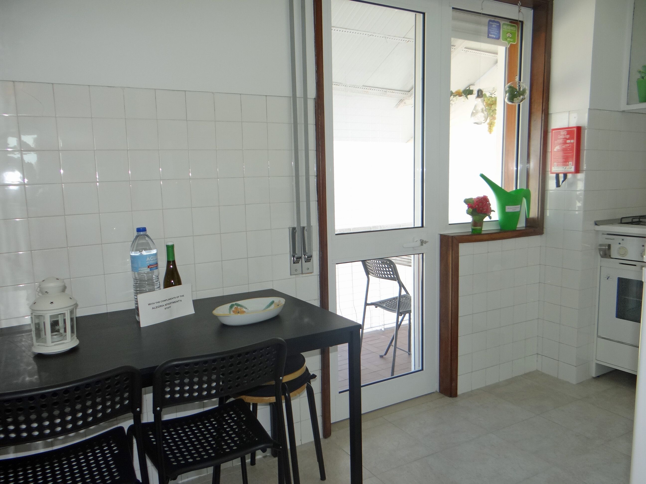 A kitchen with white tiles, a dining table with chairs, a water bottle, a candle, and a window with a view.
