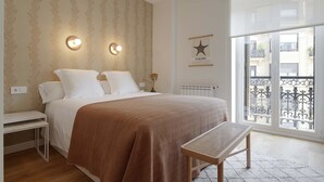 A bedroom with a large bed, bedside tables, a bench, a wall-mounted light, a radiator, and a window with a balcony view. - Belle Sebastian by FeelFree Rentals (San Sebastián)