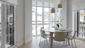 A modern dining area with a round table, six chairs, and a large window with a view of buildings. - Belle Sebastian by FeelFree Rentals (San Sebastián)