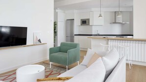 A modern living room with a sofa, a green armchair, a flat-screen TV, and a white ottoman. - Belle Sebastian by FeelFree Rentals (San Sebastián)