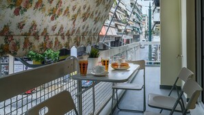 A balcony with a table set for two, a potted plant, and a view of the street below. - Modern design apartment near Acropolis (Athina)
