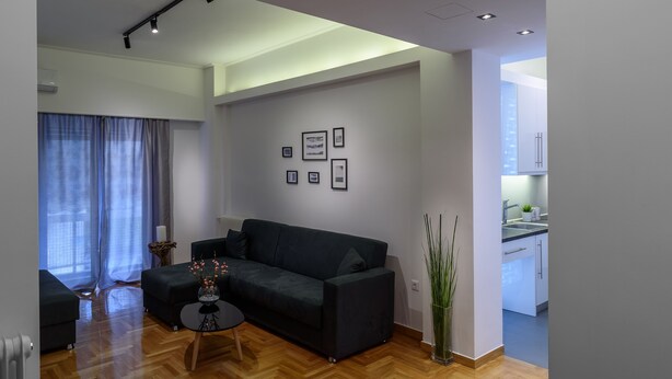 A modern living room with a dark-colored sofa, a small round table with a vase, and a large window with curtains. - Modern design apartment near Acropolis (Athina)