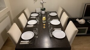 A dining table set for six with white plates, cutlery, and glasses, a small vase with flowers, and a lit candle centerpiece. - Ilmarine Apartment in city center (Tallinn)