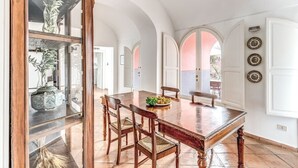 Een eetgedeelte met een houten tafel en stoelen, omringd door witte muren en gewelfde deuropeningen.