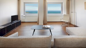 A modern hotel room with a large window offering a view of the sea, a flat-screen TV, a small table, and two sofas. - Zurriola Loft by FeelFree Rentals (San Sebastián)