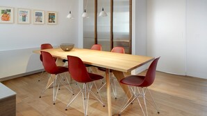 A modern meeting room with a wooden table, red chairs, pendant lights, and framed artwork on the wall. - Zurriola Loft by FeelFree Rentals (San Sebastián)