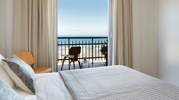 A hotel room with a bed, a chair, a small table, and a view of the beach through a balcony. - Zurriola Loft by FeelFree Rentals (San Sebastián)