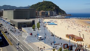 A beachside urban area with a large sandy beach, a prominent hill with a tower, and a modern building with a flat roof. - Zurriola Loft by FeelFree Rentals (San Sebastián)