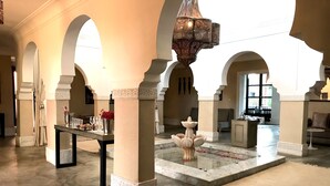 Un hall d’entrée spacieux, doté d’un sol en marbre, d’une fontaine centrale et d’une table ornée de verres et de fleurs.