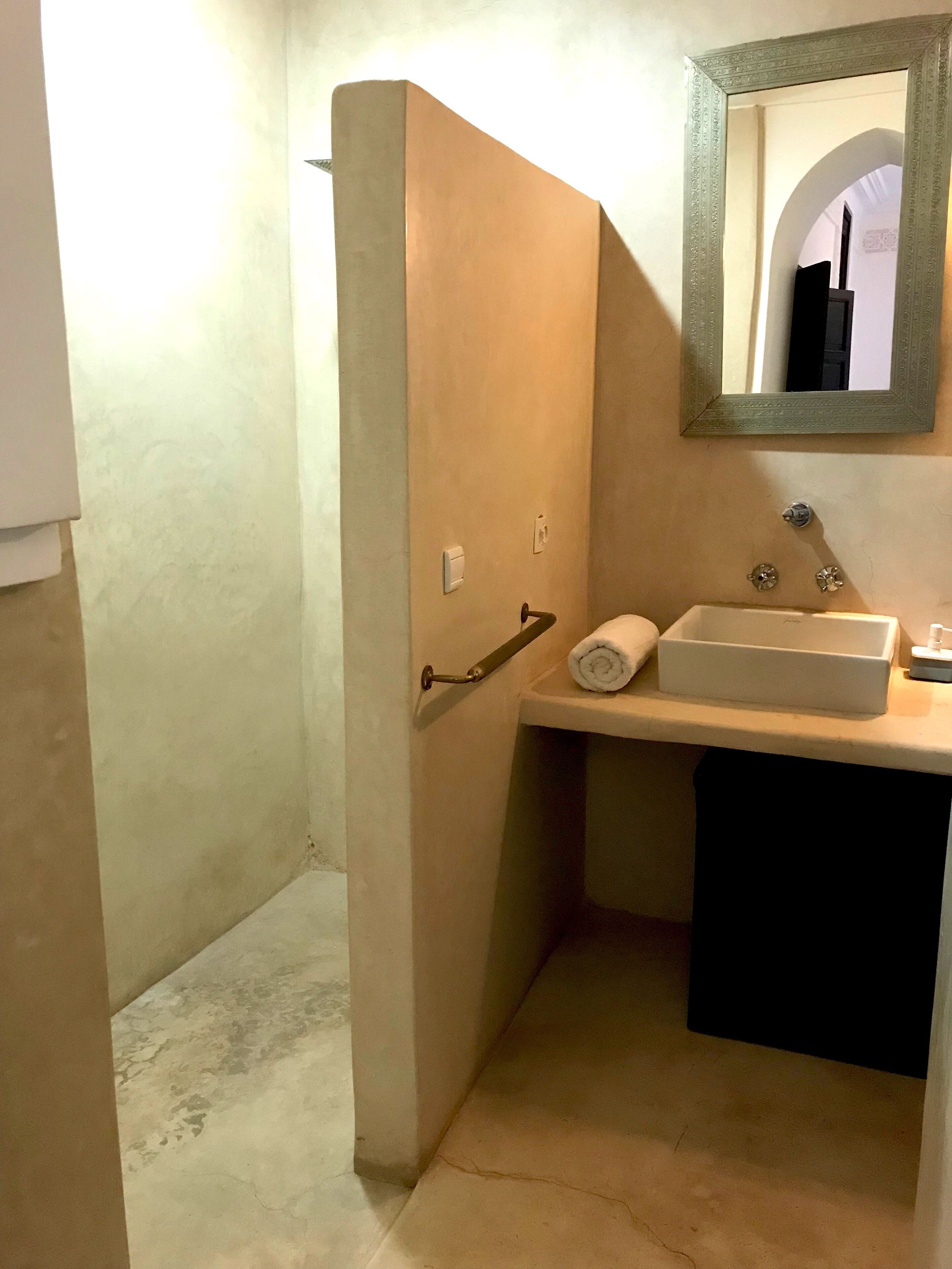 A bathroom with a beige sink, a towel, and a mirror with an ornate frame.