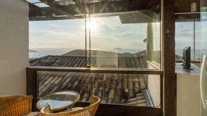 A balcony with a view of the sea and mountains, wicker furniture, and a television. - Eny Boutique Hotel (Búzios)