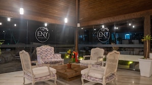 A modern interior with two upholstered chairs, a wooden coffee table, and a large window with the ENY Boutique Hotel logo. - Eny Boutique Hotel (Búzios)