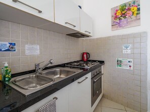 A kitchen with a double sink, a gas stove, and a kettle. There are signs on the wall and a bottle of dish soap on the counter.