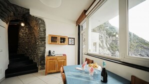 Un coin repas avec une table dressée pour deux personnes, une bouteille de vin et une vue sur un paysage montagneux par le biais d’une grande fenêtre.