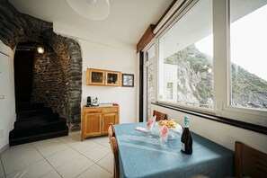 Een eethoek met een tafel gedekt voor twee personen, een fles wijn en uitzicht op een bergachtig landschap door een groot raam.