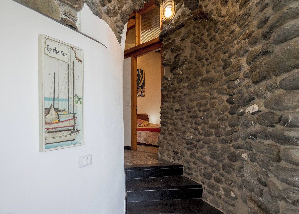 Un escalier menant à une chambre dont un des murs est en pierre et où est accrochée une image encadrée représentant un voilier.
