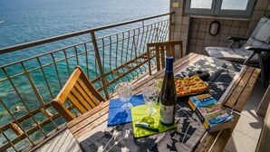 Un balcon avec vue sur la mer, une table avec une bouteille, des verres et un magazine.