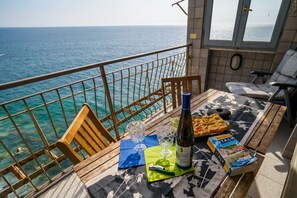Een balkon met uitzicht op zee, een tafel met een fles, glazen en een tijdschrift.