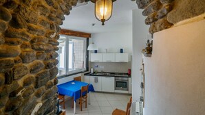 Une cuisine avec des meubles blancs, une table bleue et un mur en pierre.
