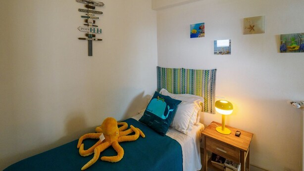 Une chambre à coucher avec un lit, une table de chevet avec une lampe, un mur orné d’une affiche et une fenêtre avec des rideaux.