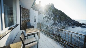 Un balcon avec vue sur la mer, un mur en pierre et une table avec des chaises.