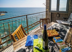 Un balcón con vista al mar, una mesa con una botella, vasos y una revista.
