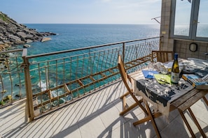 Un balcon avec vue sur la mer, une table avec une bouteille et une chaise.
