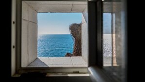 Une fenêtre donnant sur l’océan et une falaise rocheuse.