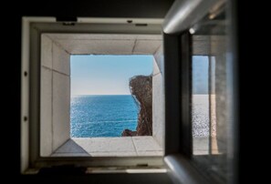 Une fenêtre donnant sur l’océan et une falaise rocheuse.