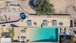 An aerial view of a resort with a large swimming pool, sun loungers, and a small hot tub.