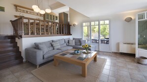 A spacious living room with a grey sofa, a wooden coffee table, and a staircase leading to an upper level.