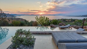 An infinity pool with lounge chairs and a view of the sea at sunset.