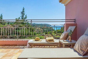 A balcony with a view of a coastal landscape, a table with a hat and books, and a chair with a cushion.