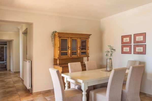 A dining area with a white table and chairs, a wooden cabinet, and framed pictures on the wall.